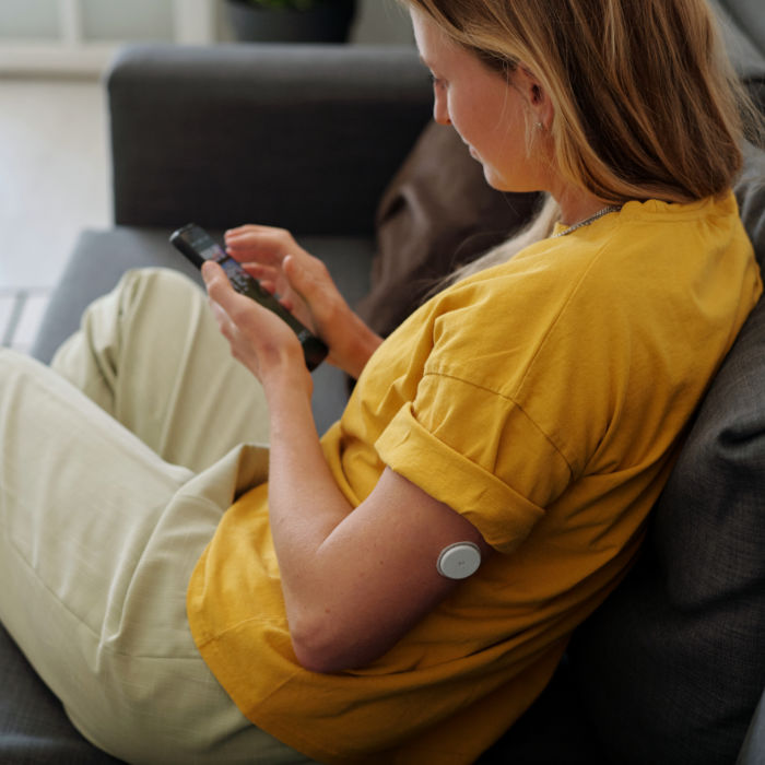 Woman with CGM Sitting on Sofa with Smartphone
