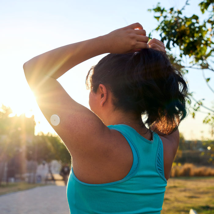 Young sportswoman tying hair with glucose sensor or monitor at sunset in park
